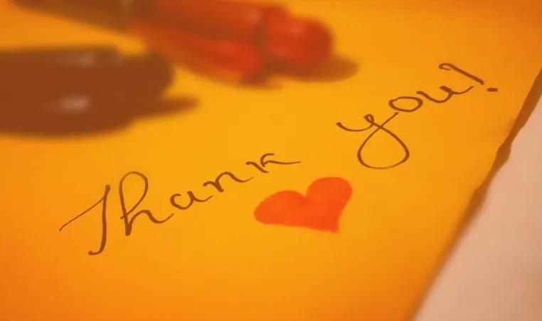 Photo shows handwritten "thank you" with pens on yellow paper