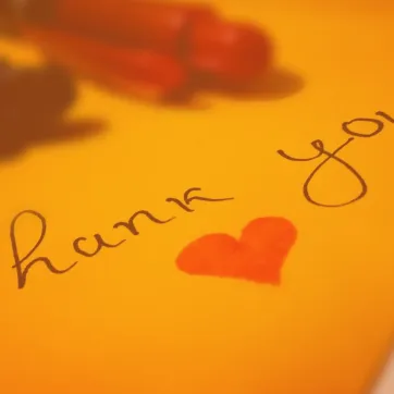 Photo shows handwritten "thank you" with pens on yellow paper